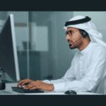 مندوب مبيعات اتصالات يتحدث عبر سماعة الرأس إلى العميل بينما يوجه نظره إلى شاشة الحاسوب