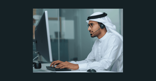 مندوب مبيعات اتصالات يتحدث عبر سماعة الرأس إلى العميل بينما يوجه نظره إلى شاشة الحاسوب